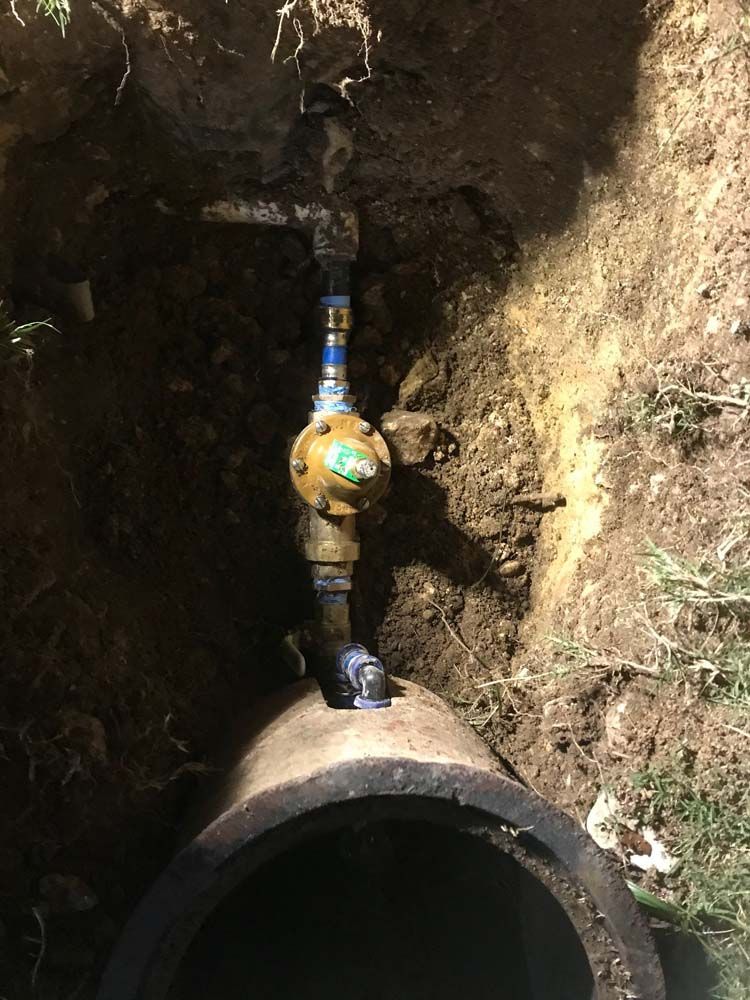 A water meter is sitting in the dirt next to a pipe.