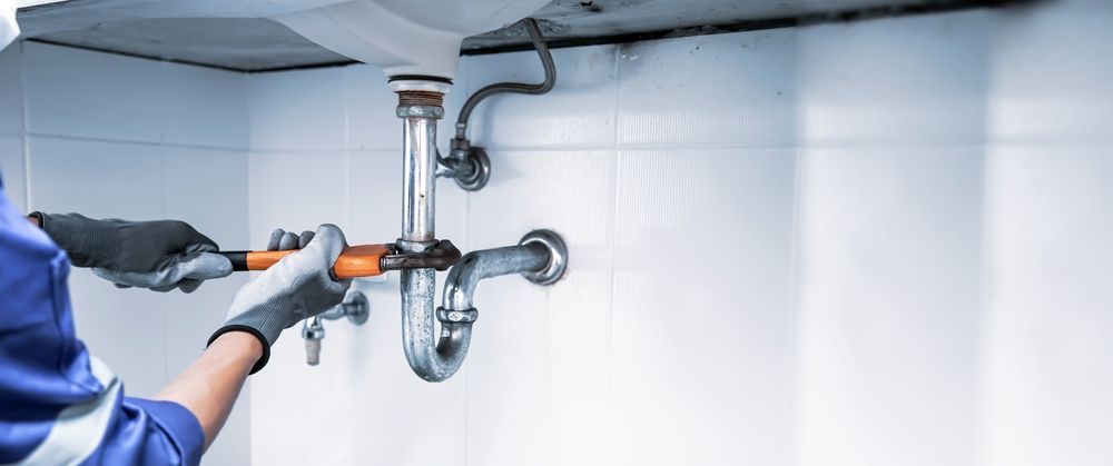 A plumber is fixing a sink pipe with a wrench.