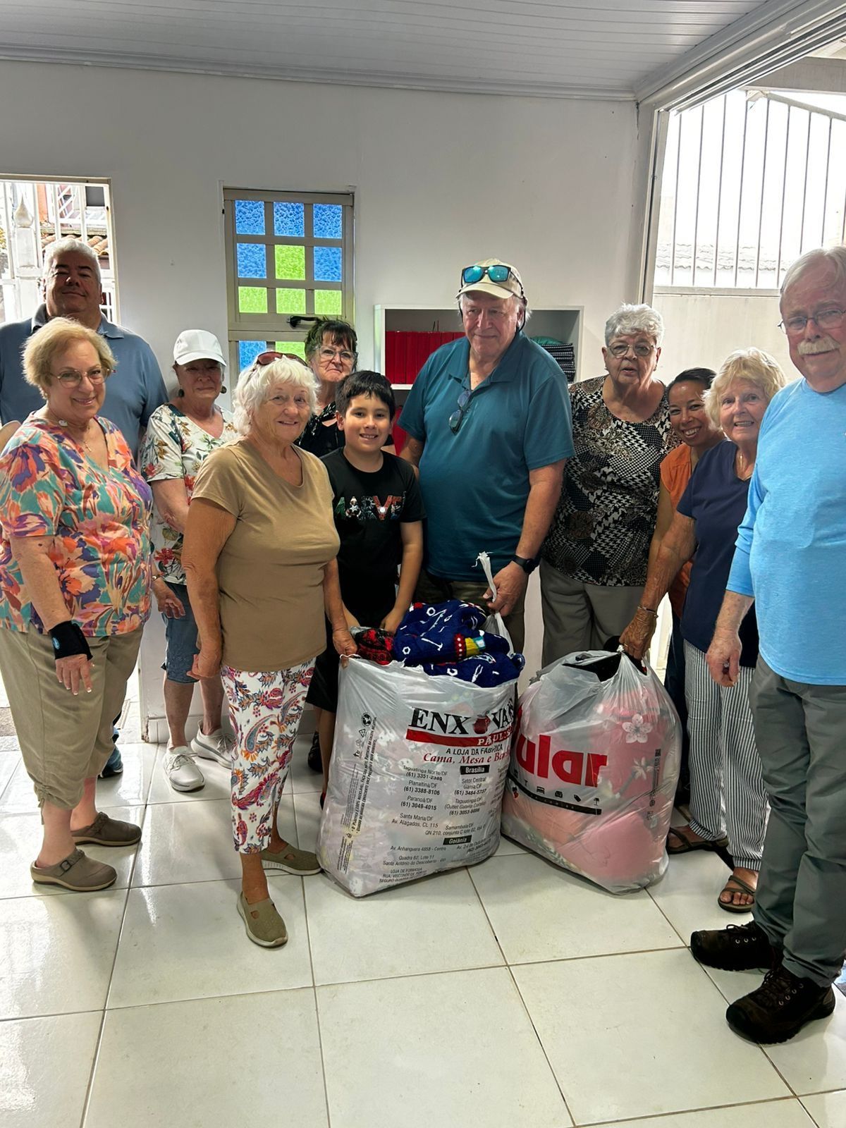 Group of people with donations in bags, indoors. Some are smiling, likely a volunteer or charity event.