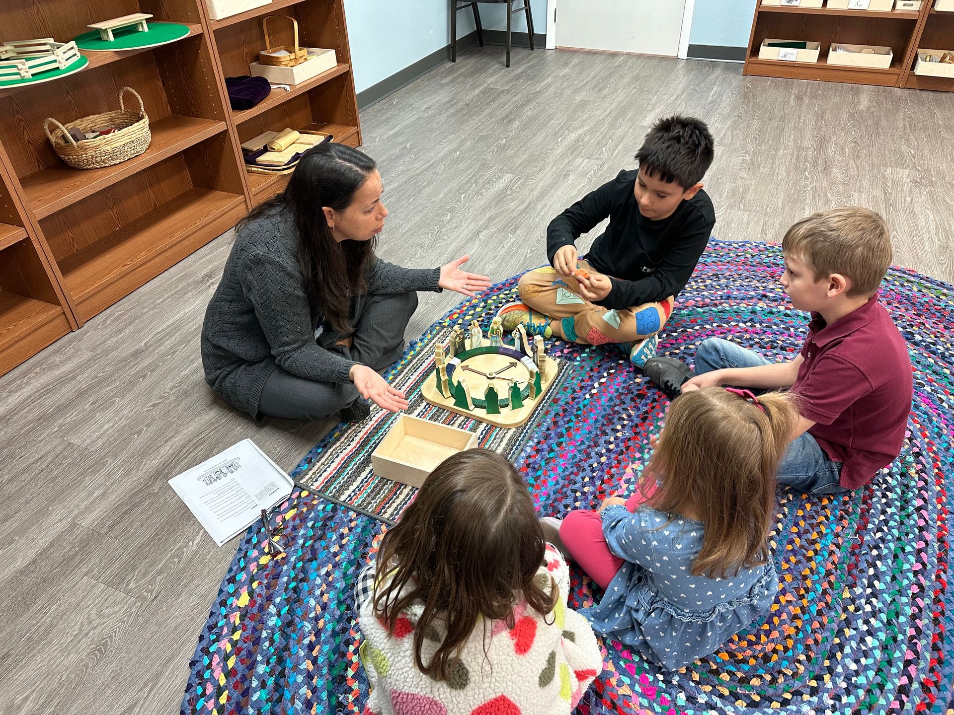 A group of children are sitting on the floor in a circle with a teacher.