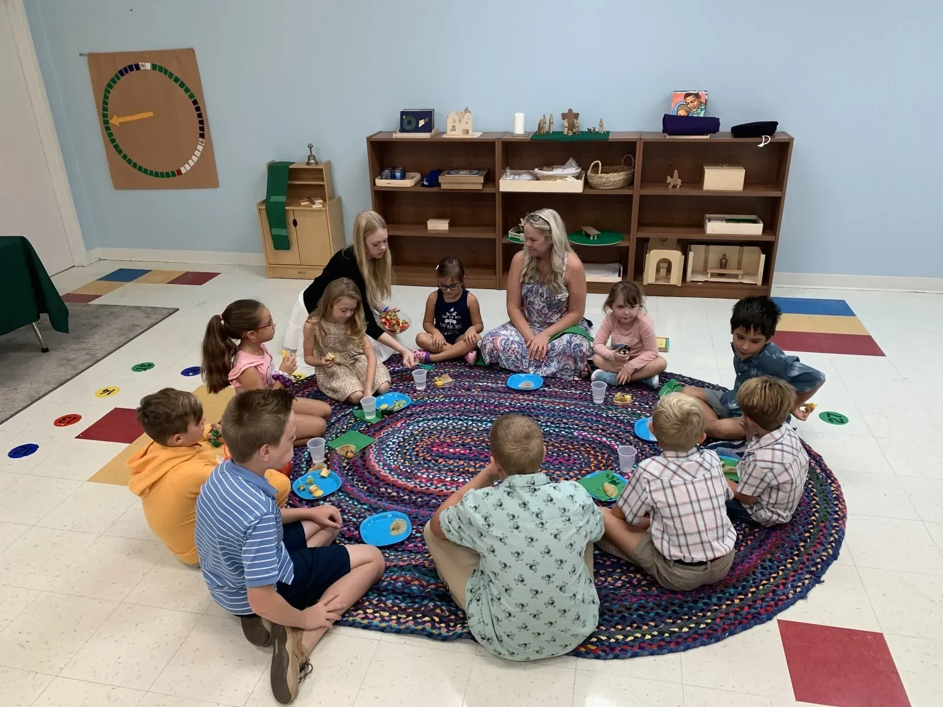 A group of children are sitting in a circle on a rug.