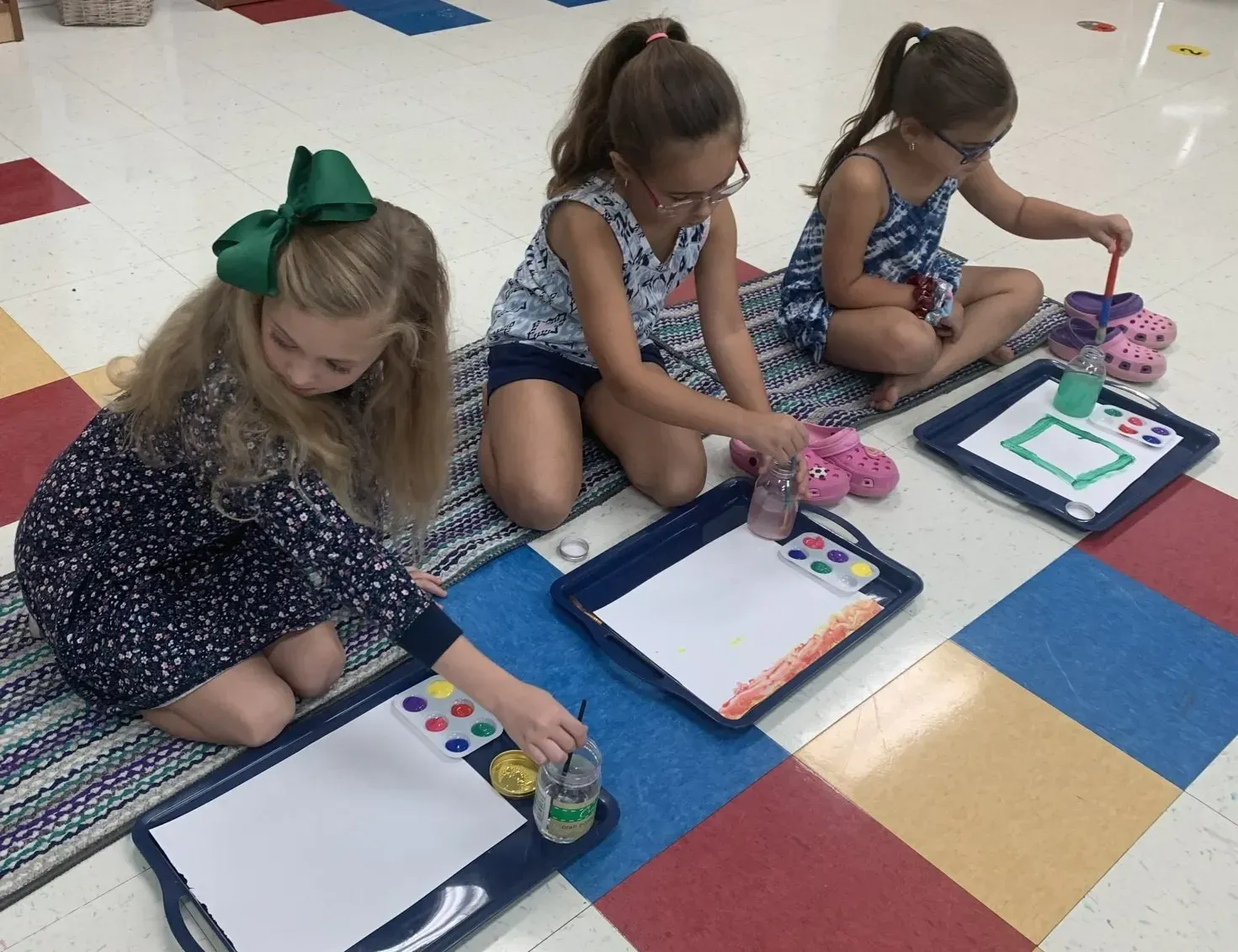 Three little girls are sitting on the floor painting