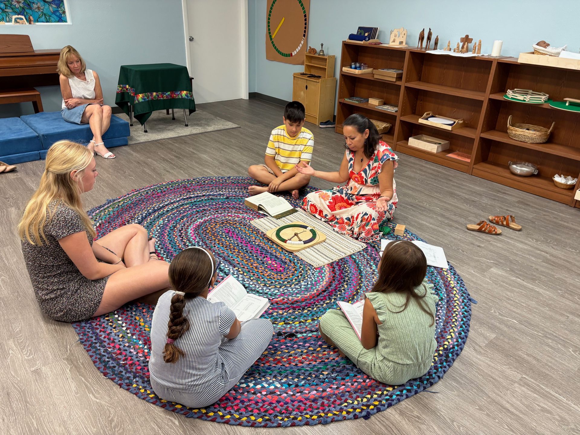 Group of students and a teacher in a circle on a rug, reading. Classroom setting.