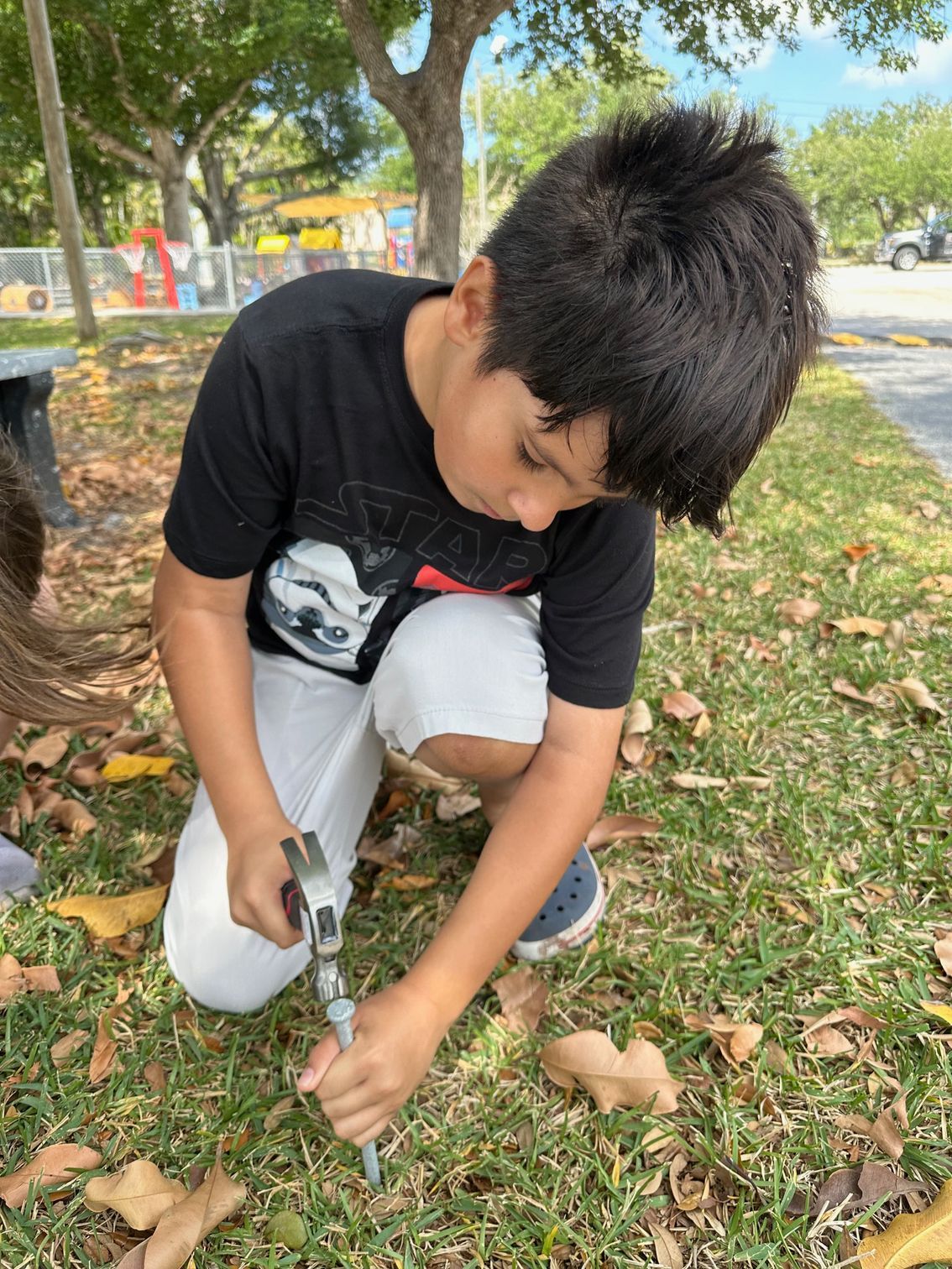 A young boy is kneeling down in the grass holding a pair of scissors.