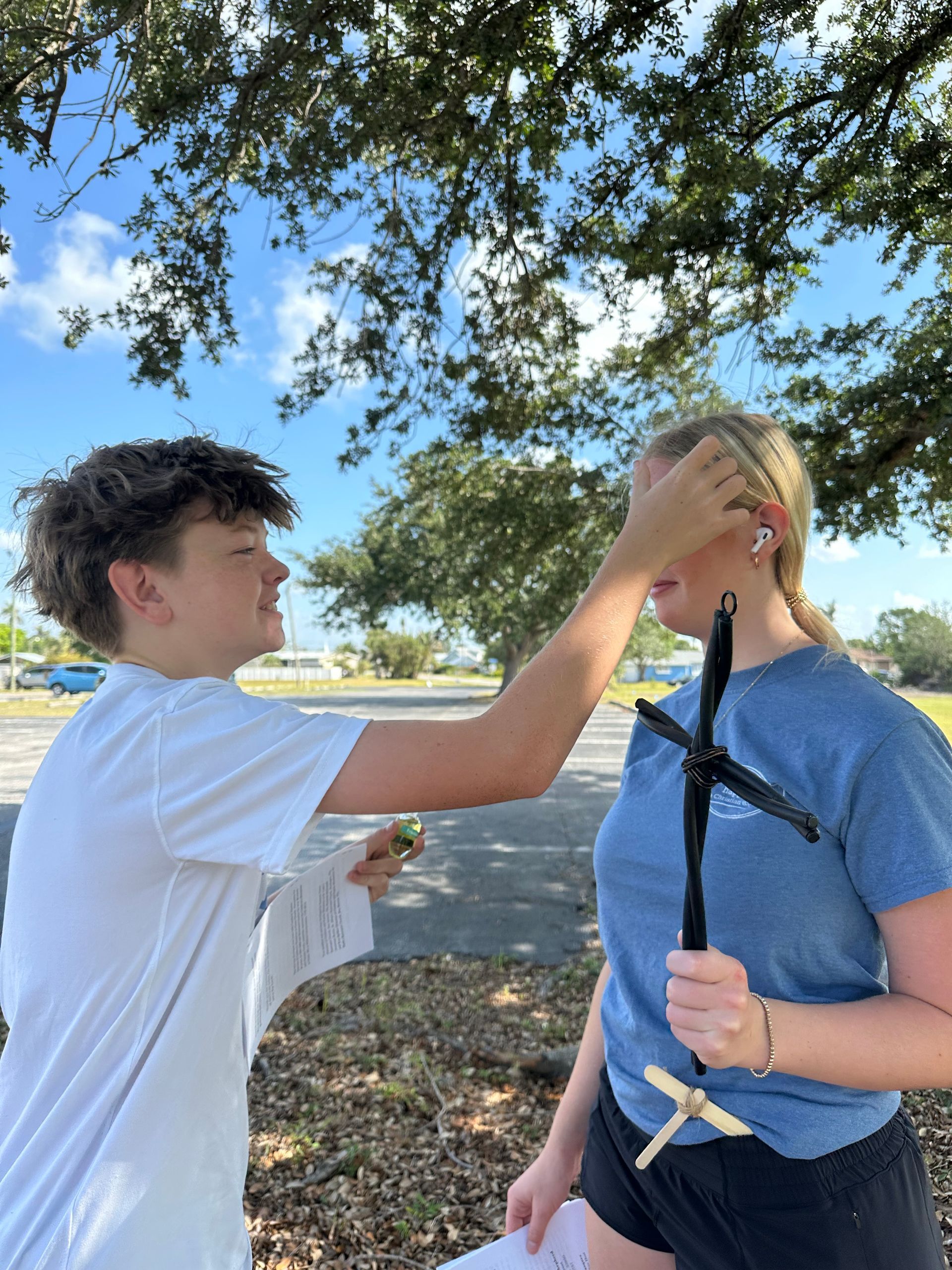 A boy is putting a cross on a girl 's forehead.