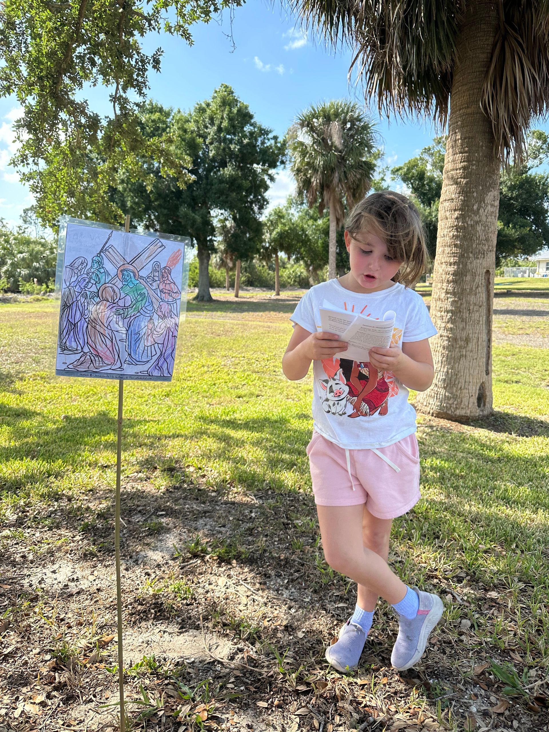 A little girl is reading a book in a park.