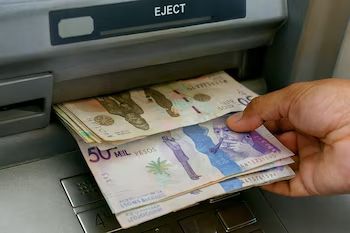 Una mano saca un fajo de billetes colombianos de 50.000 pesos de un cajero automático.