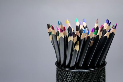 Un grupo de lápices de colores afilados, con cuerpo negro, sostenidos en un vaso de malla