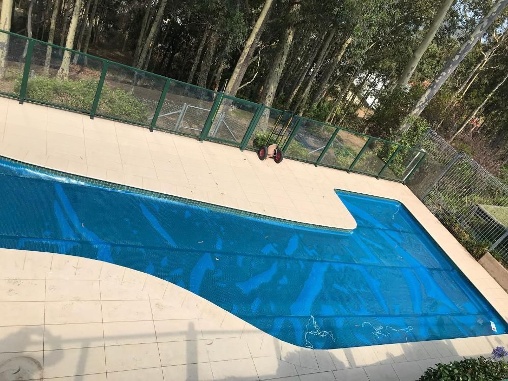 A Large Swimming Pool Surrounded By Trees and a Fence —  Pool Services in Newcastle