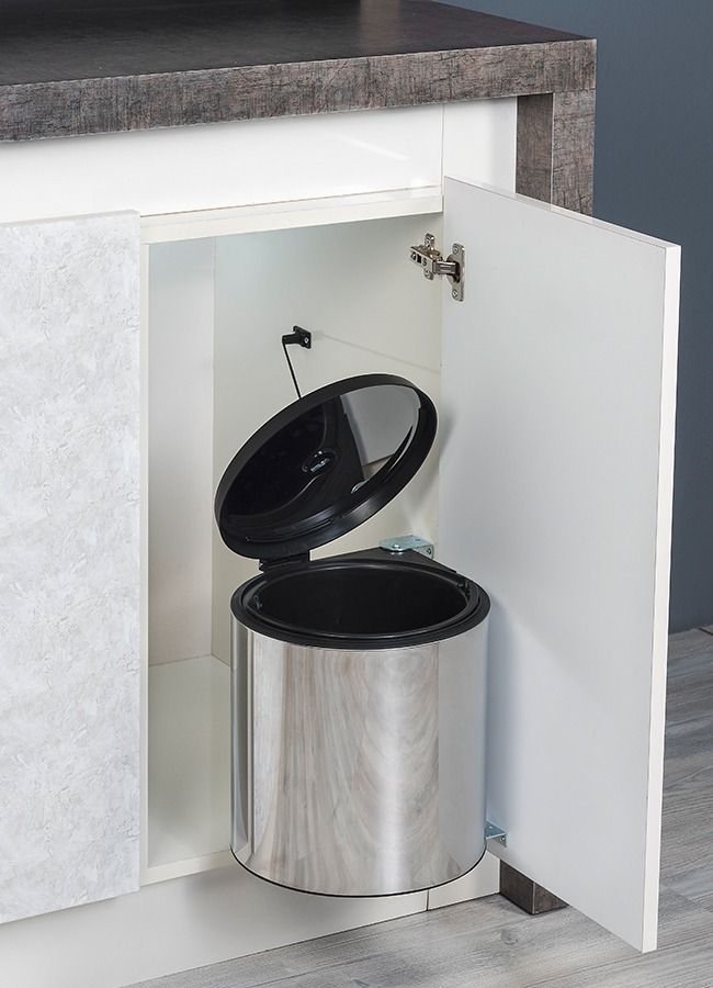 Cubo de basura de acero inoxidable dentro de la puerta abierta de un armario. La tapa está abierta.