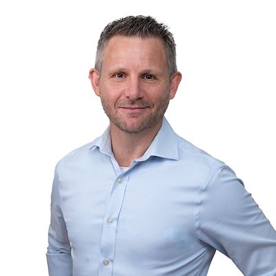 Man in light blue shirt smiles at the camera, against a white background.