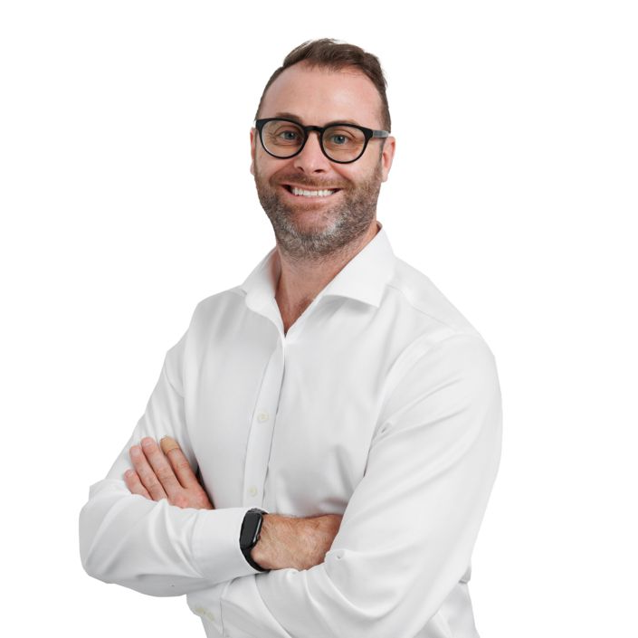 Man with glasses, arms crossed, smiling. Wearing a white button-down shirt.