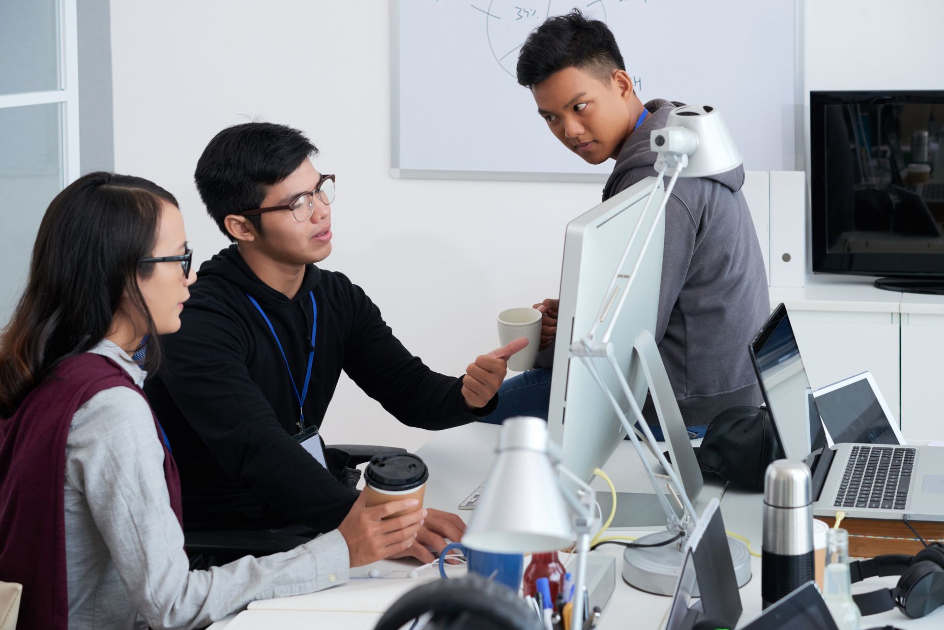 Three people collaborating at a desk, with one pointing at a computer screen while another watches from behind.