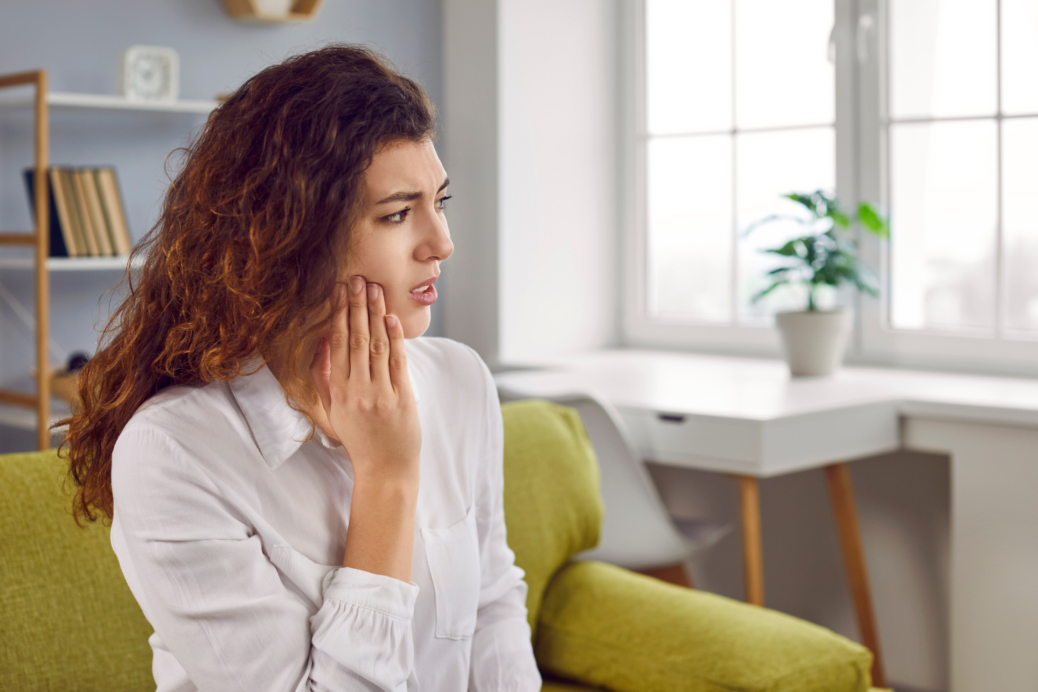 a woman is sitting on a green couch with a toothache