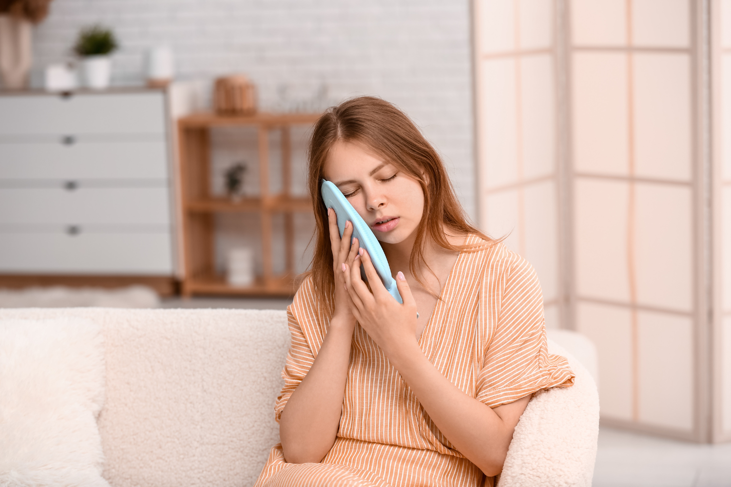 a woman sitting on a couch with a blue ice pack on her face