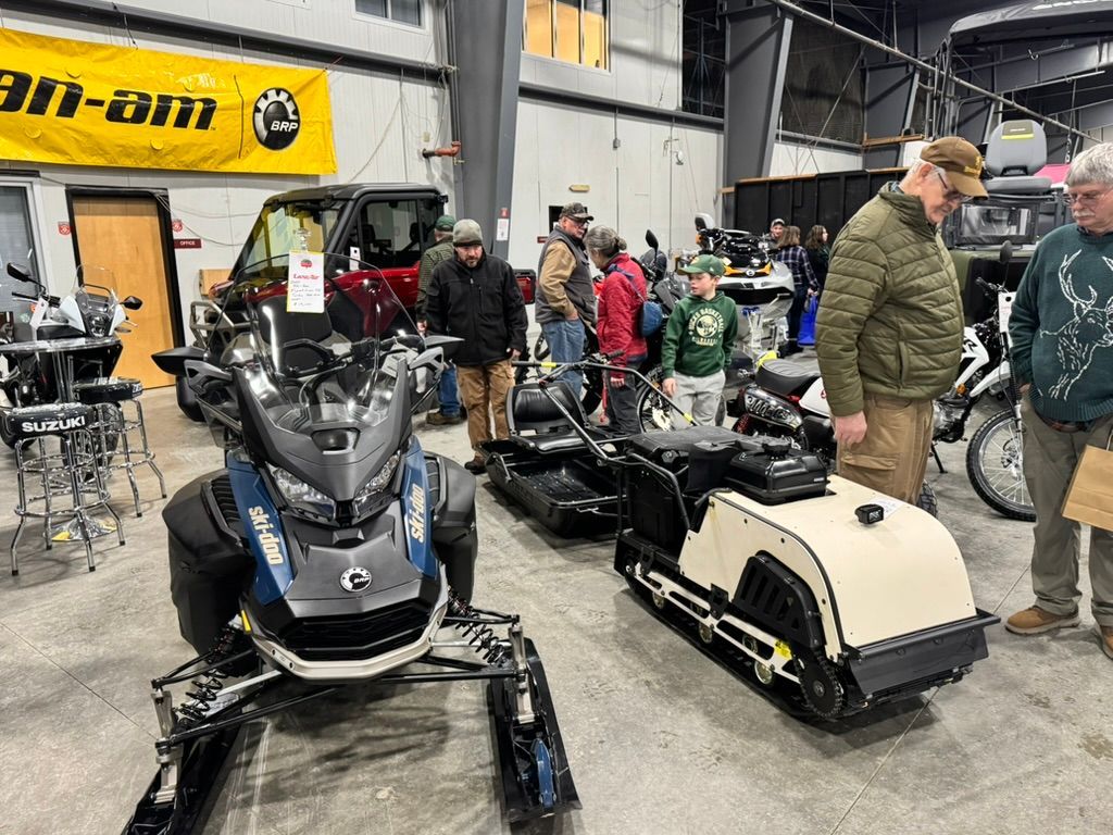 Snowmobiles on display, people browsing at an indoor event.