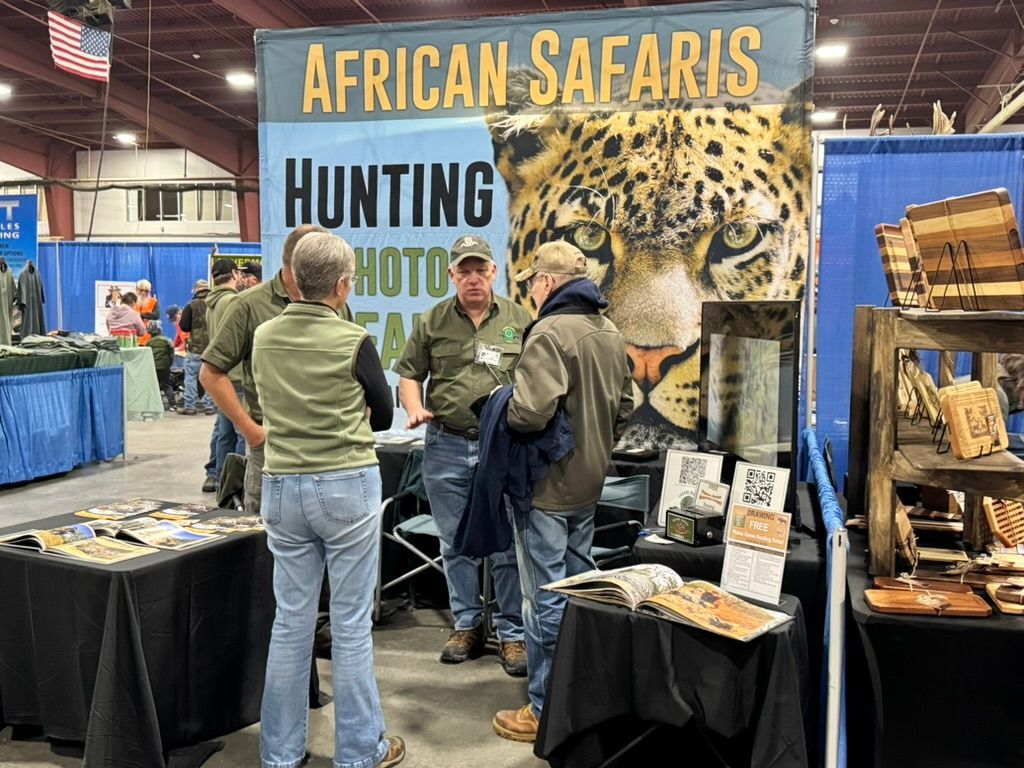 African Safaris booth at an exhibition. People converse in front of a banner featuring a leopard.