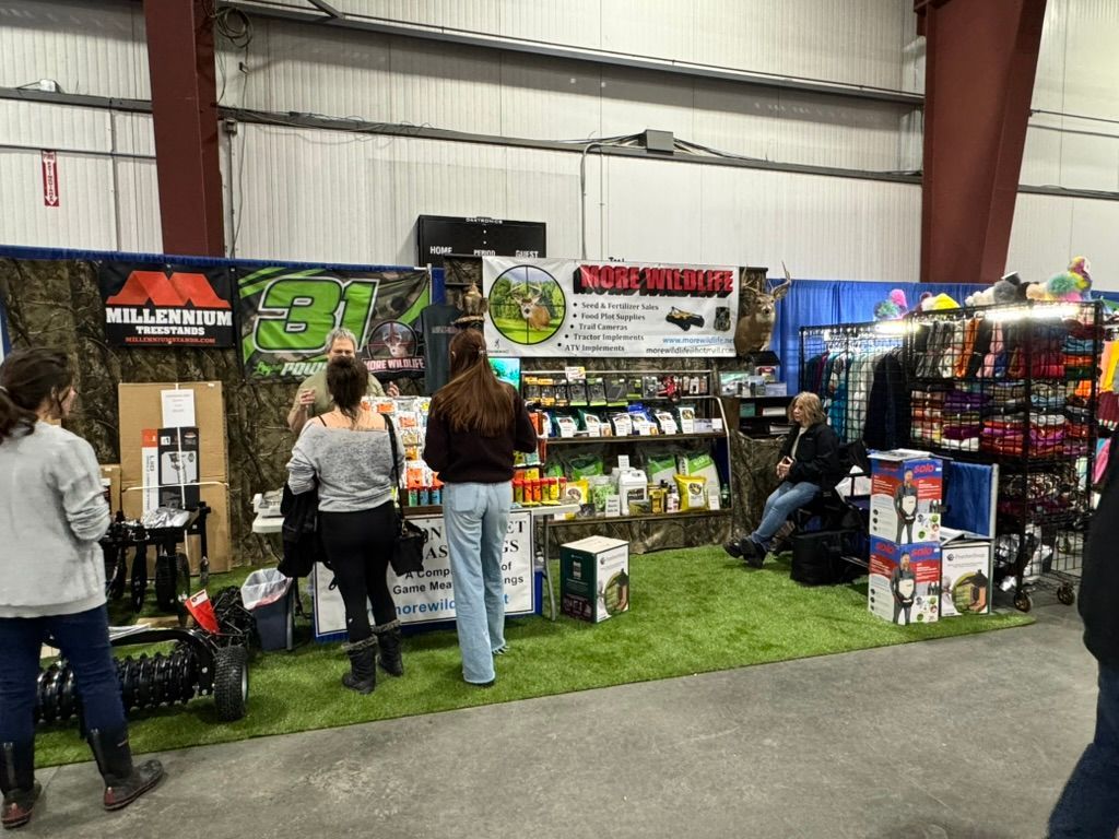 People browse a vendor booth at a trade show. The booth sells hunting and outdoor supplies.