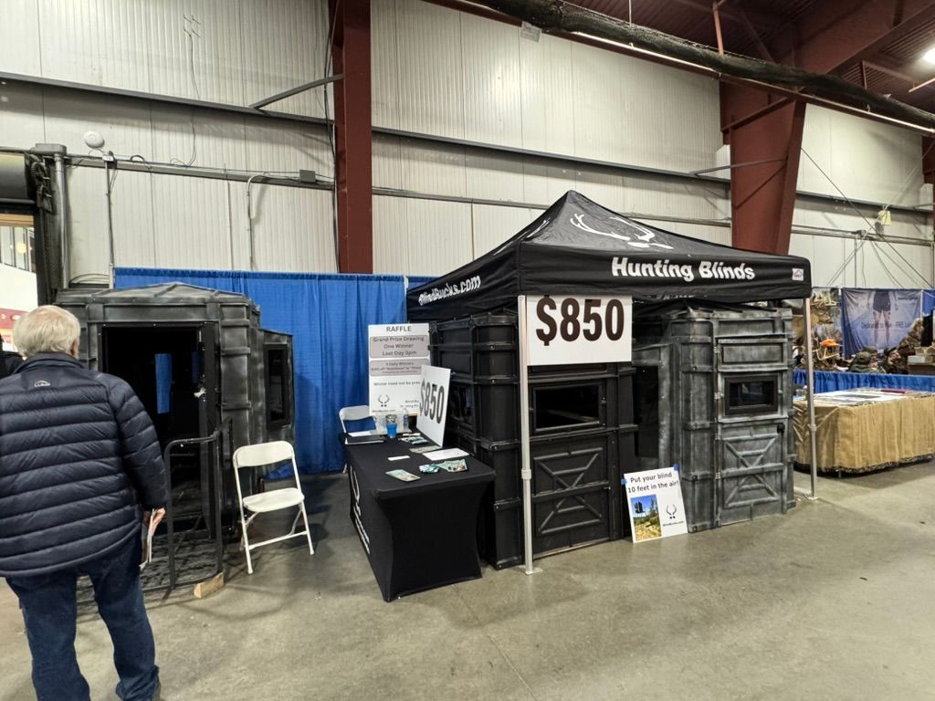 Hunting blind display at a trade show: black structures, tent, price tag ($850), person looking at the booth.