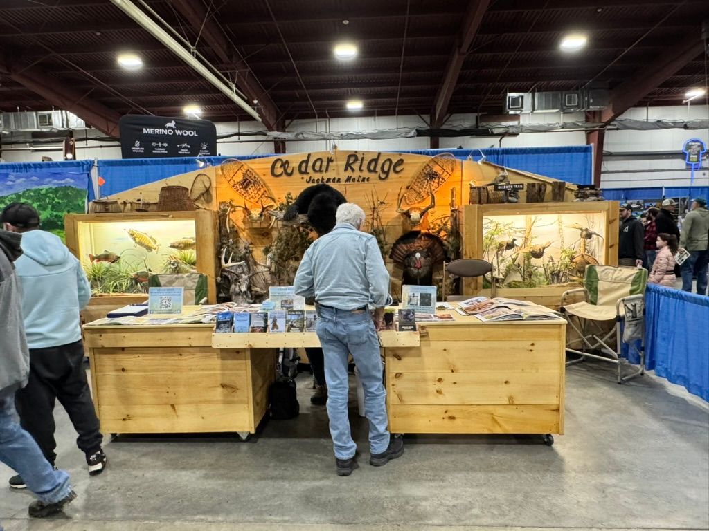 Booth for Cedar Ridge Outdoors at a fair. Man looks at display of fish and other wildlife.