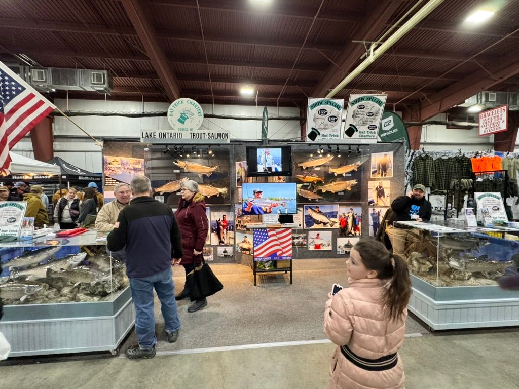 People at a fishing expo booth with fish displays, flags, and signs.
