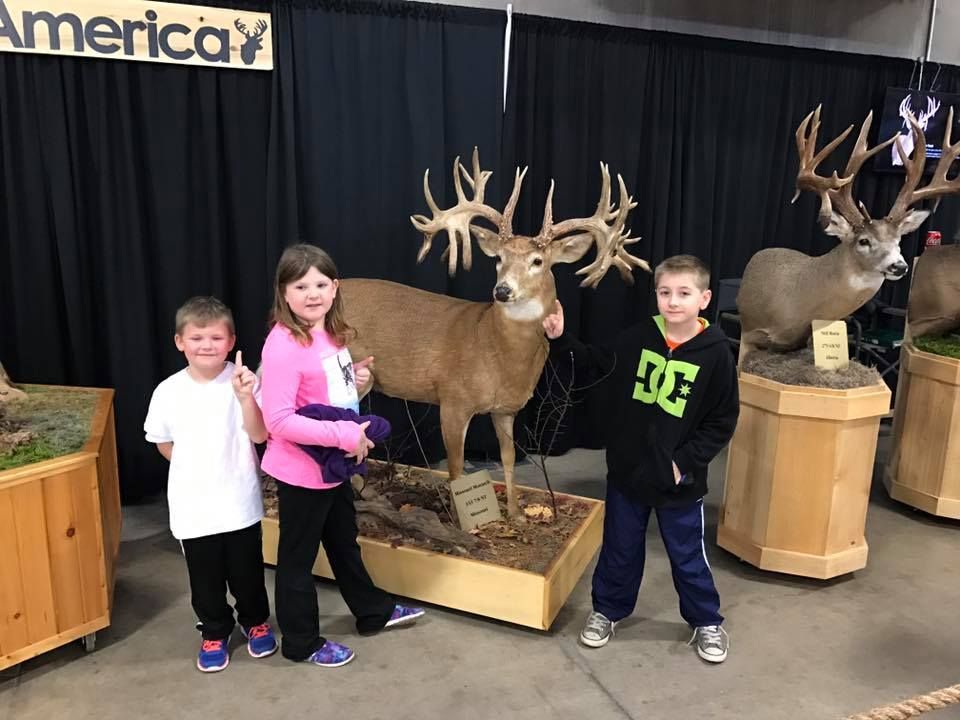 Three children are standing in front of a stuffed deer.