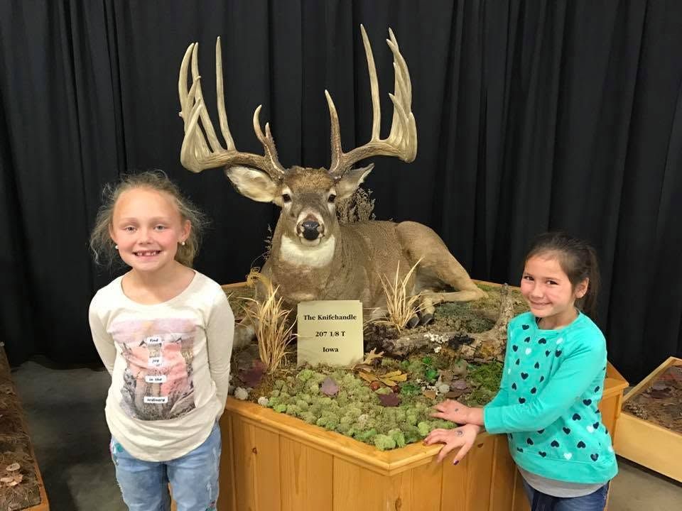 Two young girls are standing next to a stuffed deer.
