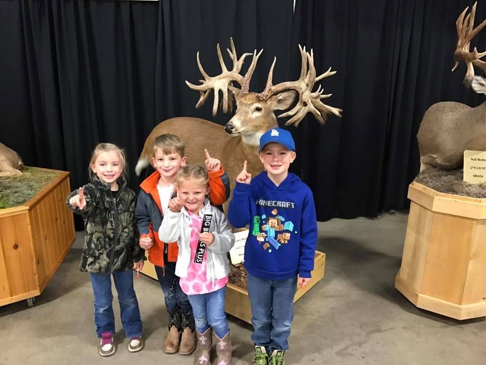 A group of children are posing for a picture in front of a stuffed deer.