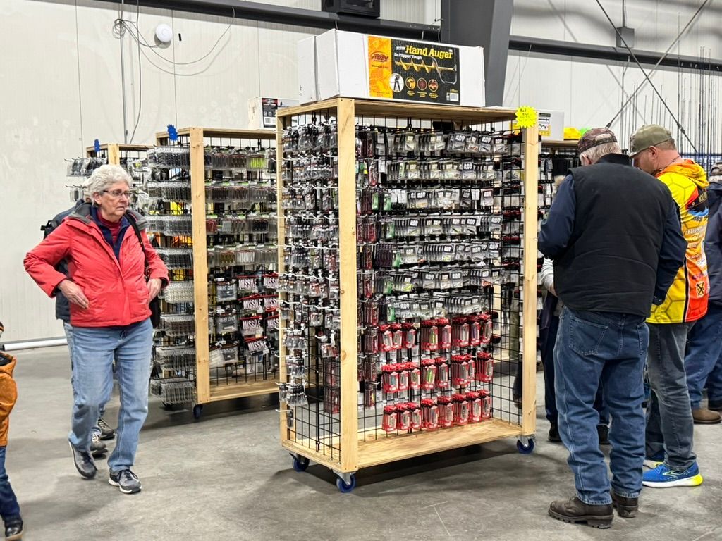 People browsing fishing lures at a trade show; displays on wheels.