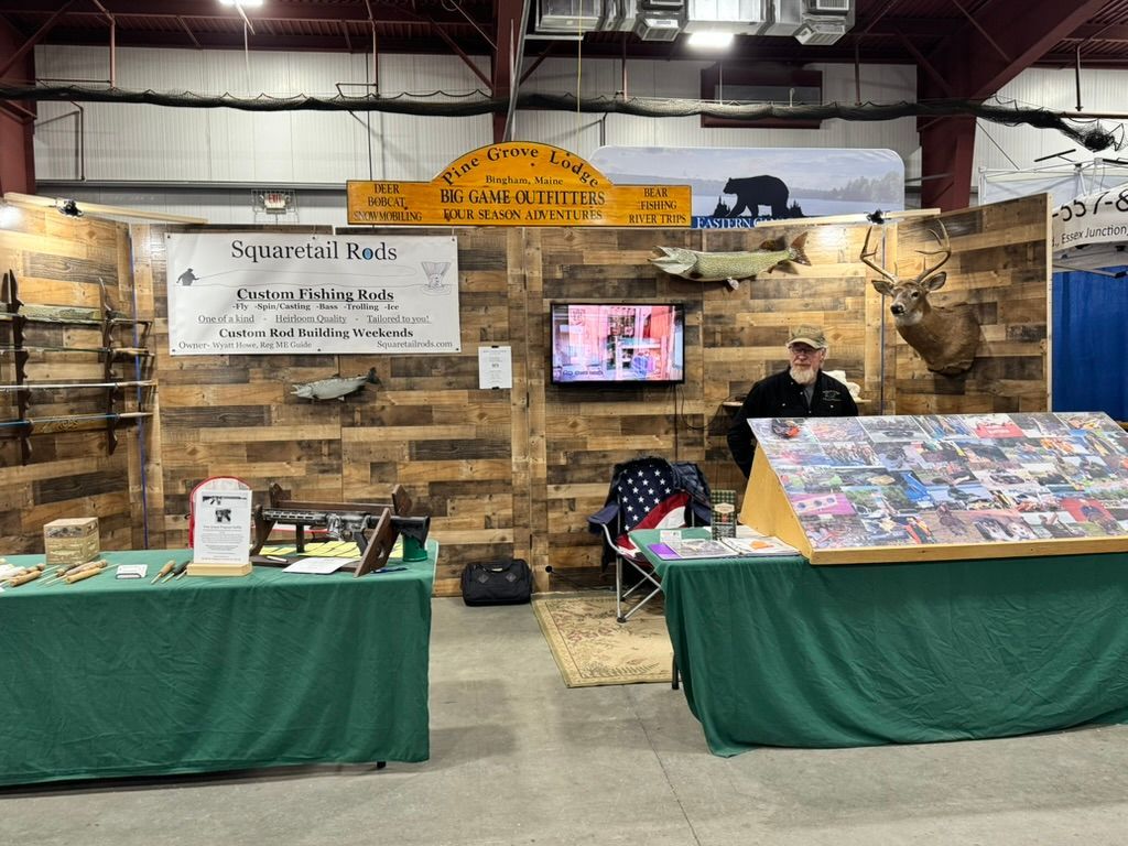 Booth at an event. A man stands behind a table displaying wildlife products, with taxidermy and a TV.