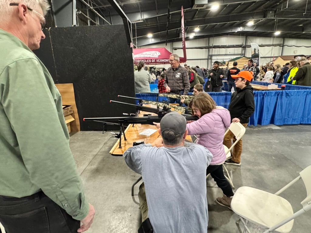 People at a gun show, looking at and handling firearms on display at a table indoors.