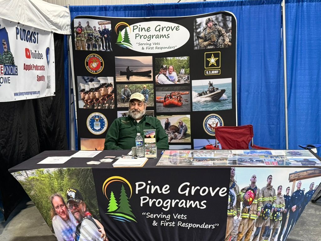 Man at Pine Grove Programs booth. Logos and photos about veterans and first responders are displayed.