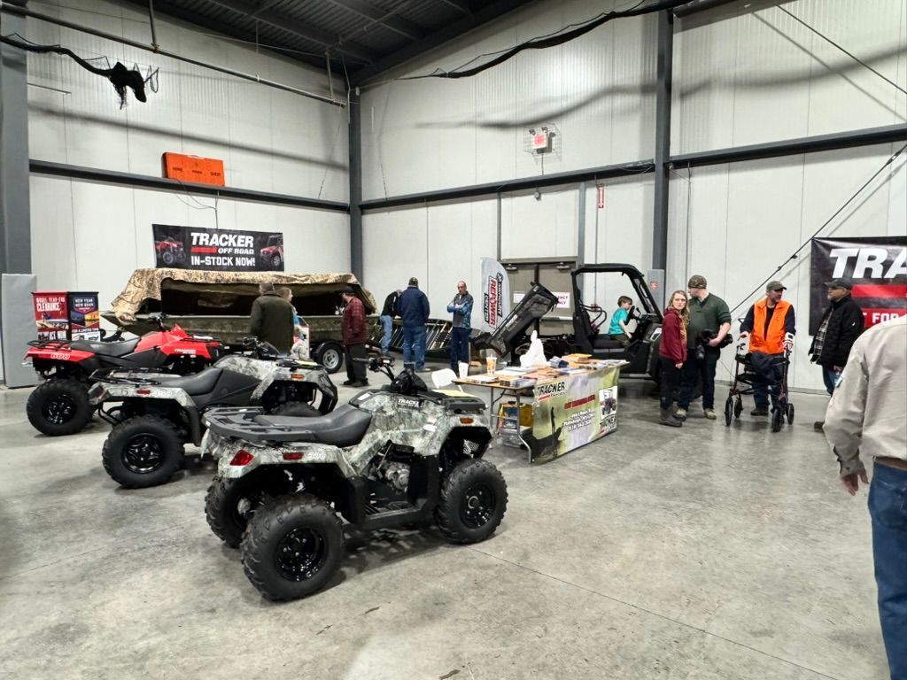 A display of ATVs and utility vehicles at an indoor event, with people browsing the products.