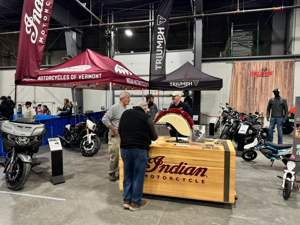 Motorcycle show with Indian and Triumph booths. People browse bikes and displays inside a large building.