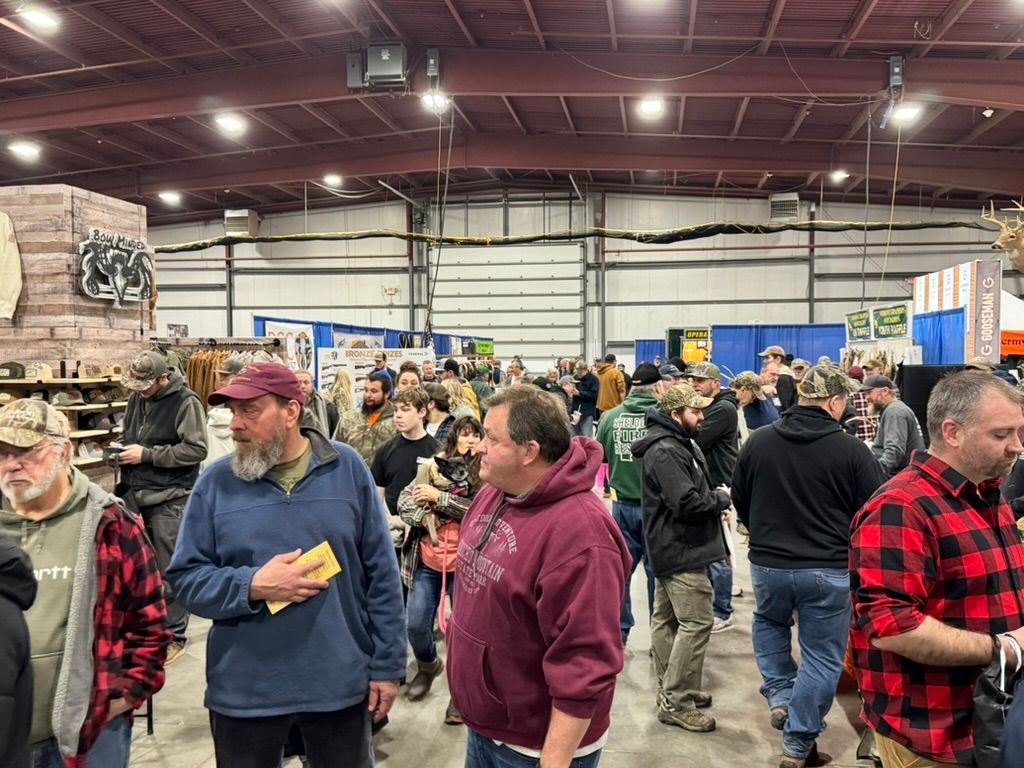 Large crowd at an indoor event, likely a fair or expo. People milling about, stalls in the background.