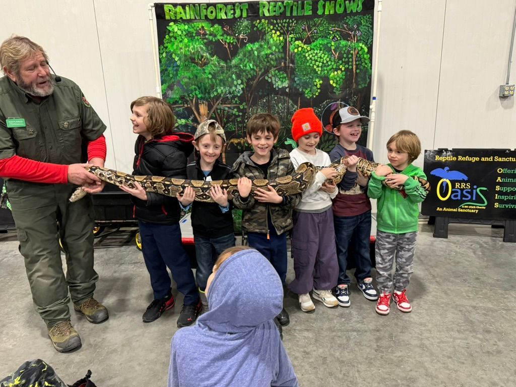 A man and six children holding a large snake at a reptile show.