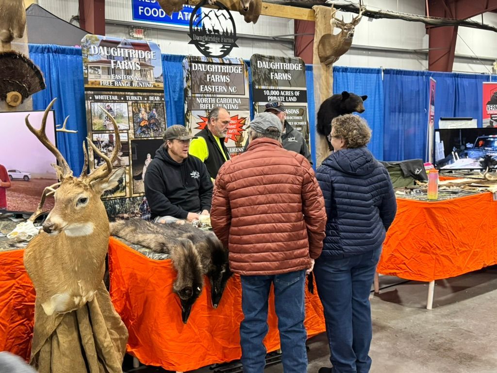 People at a hunting expo booth with animal mounts, fur, and display items.