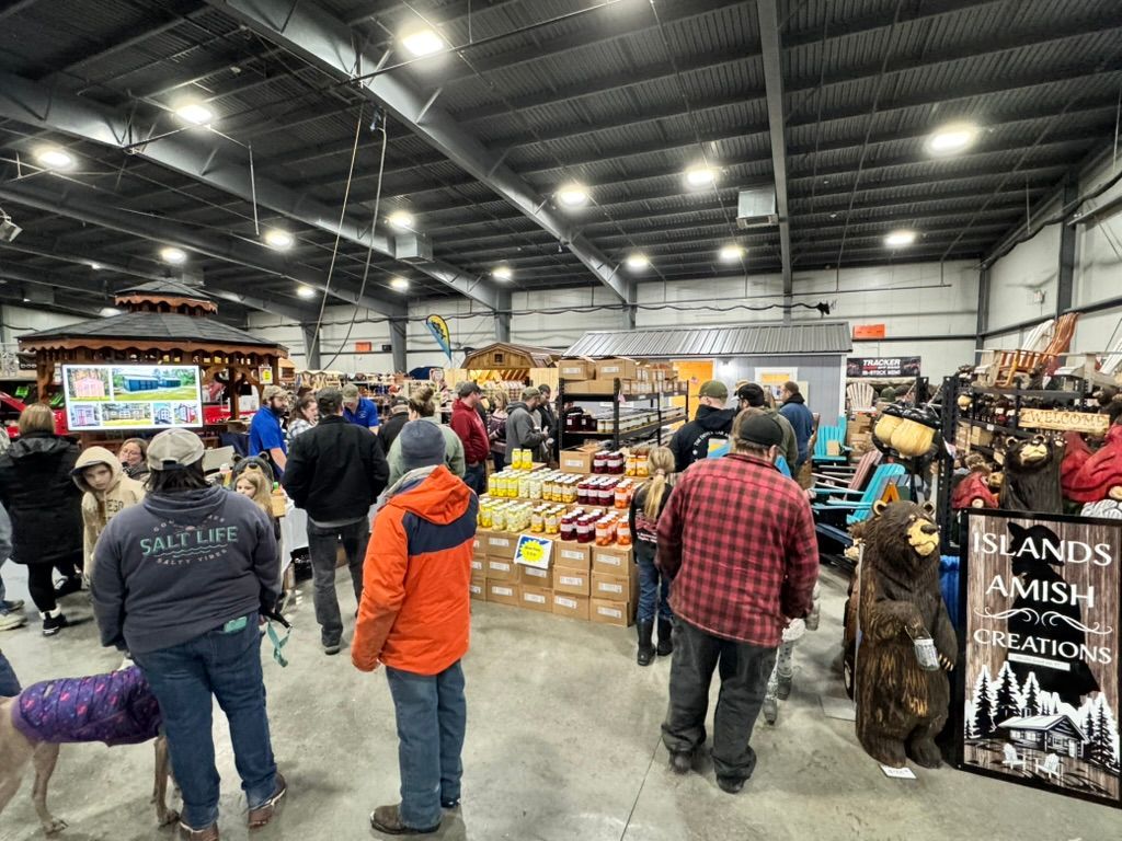 People browsing vendors' booths at an indoor event, with merchandise and a bear carving on display.