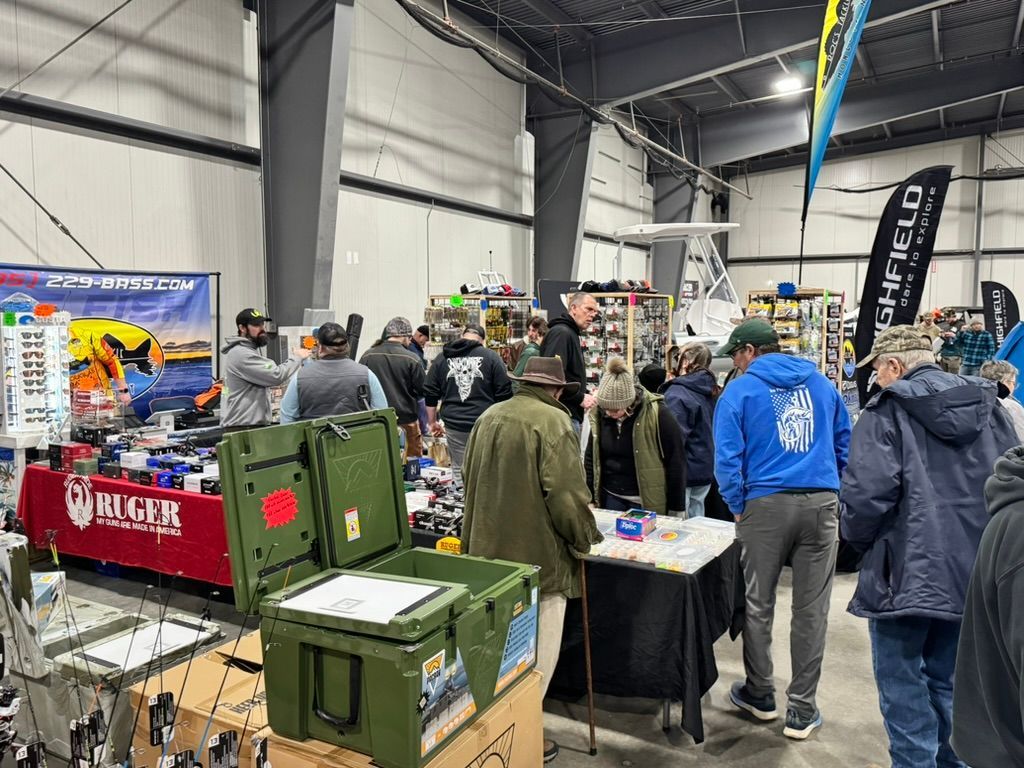 A crowded indoor event with vendors and shoppers; fishing gear on display.