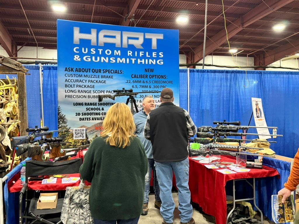 Booth for Hart Custom Rifles at a gun show with customers viewing rifles and a blue backdrop.