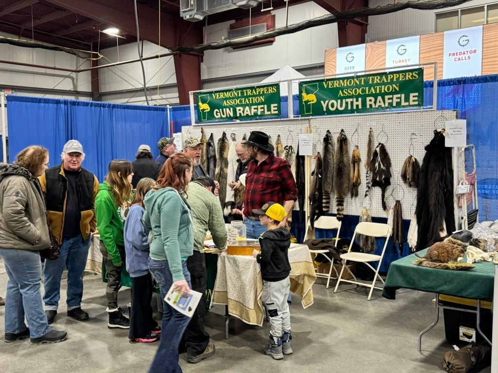 People at a vendor booth with animal pelts and signs for raffles at an event.
