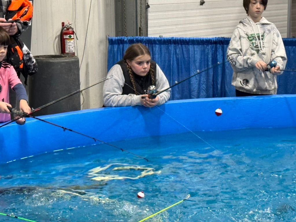 Children fishing in a blue pool. Girl watches her line, others hold rods.