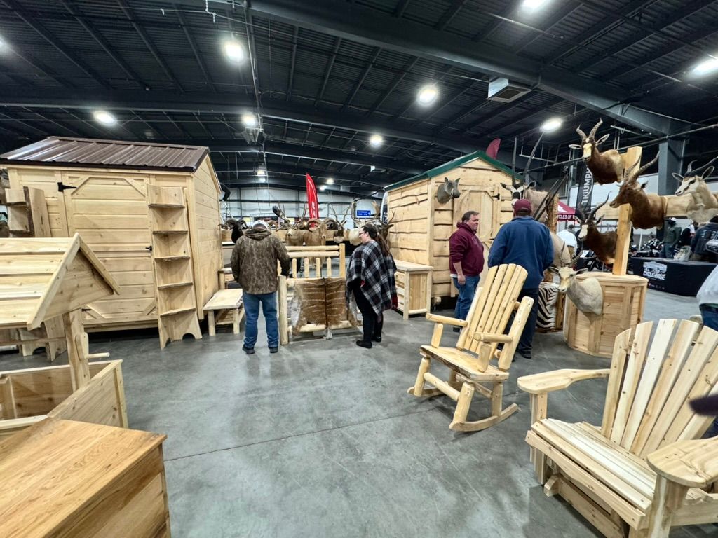People browsing rustic wooden furniture and cabins at an indoor show.