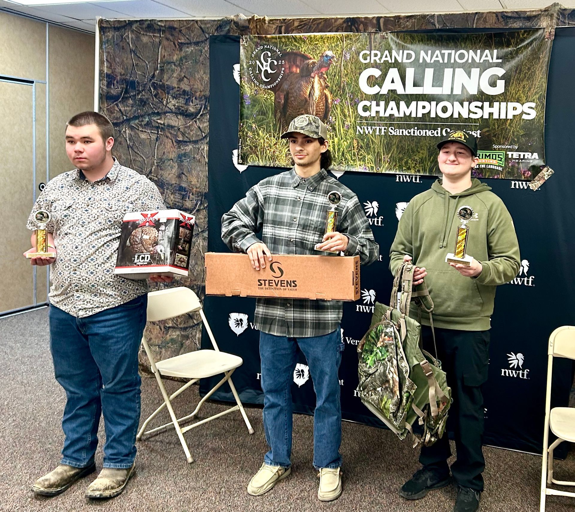 Three people holding awards stand in front of a backdrop reading 