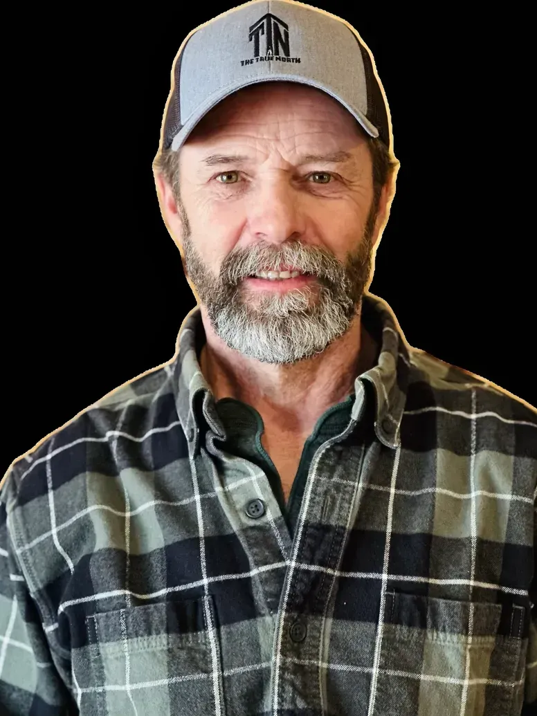 Man with a beard, wearing a grey baseball cap and a plaid shirt, smiling.