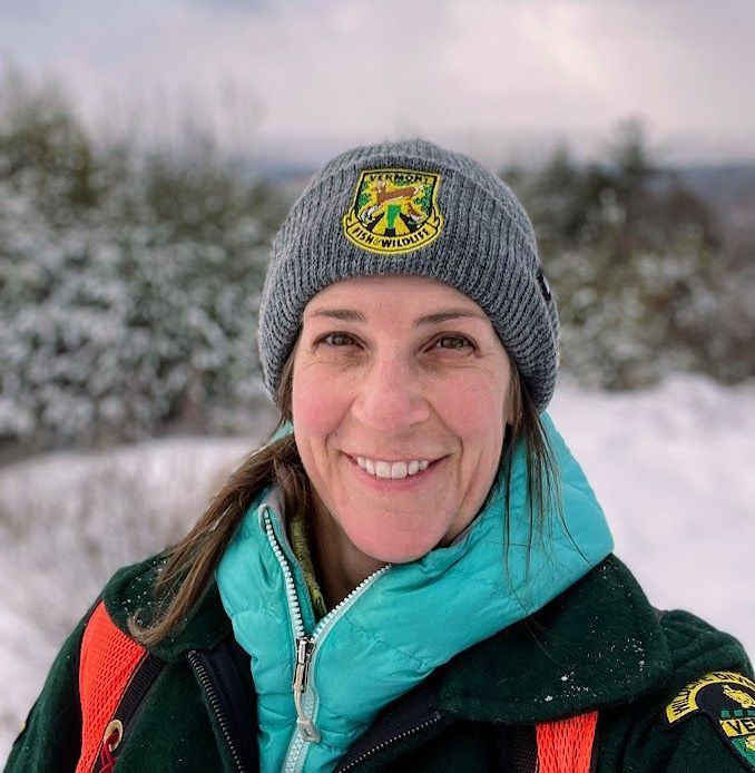 A woman wearing a hat and a jacket is smiling in the snow.