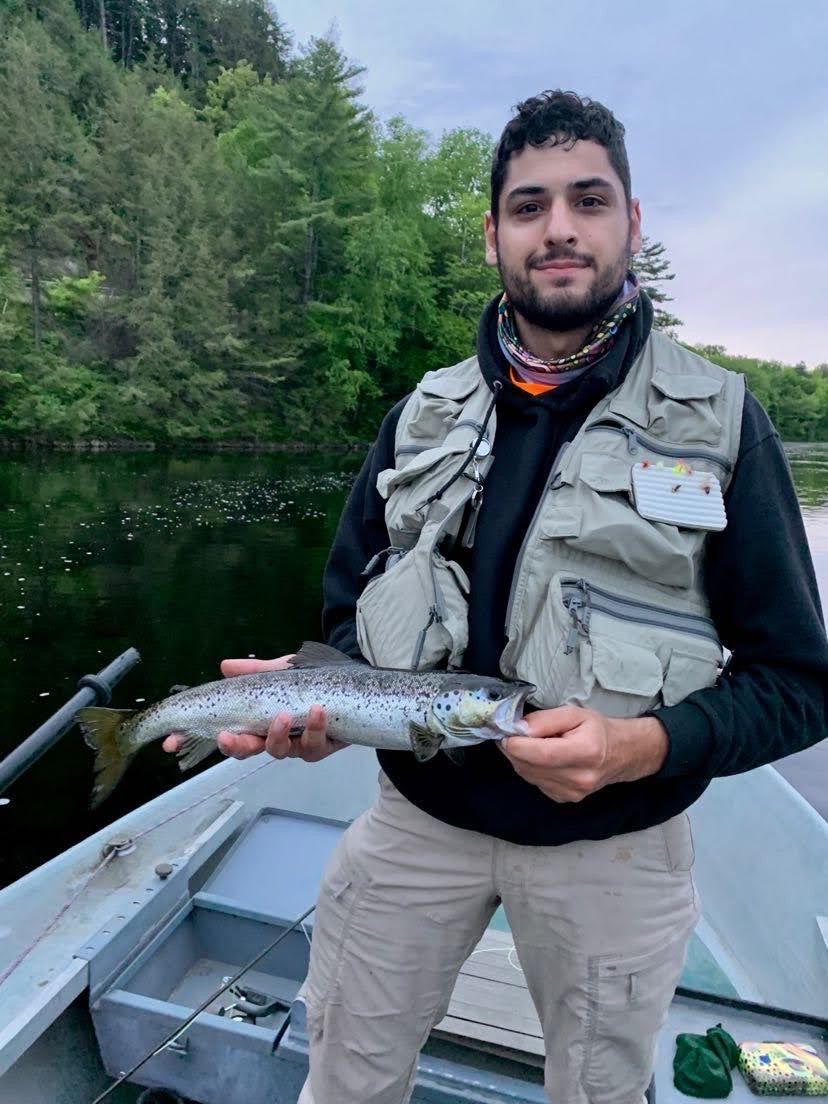 Man in a fishing vest holding a brown trout in a boat on a lake.