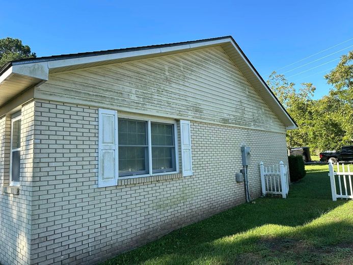 A white brick house with white shutters and a white fence in front of it.