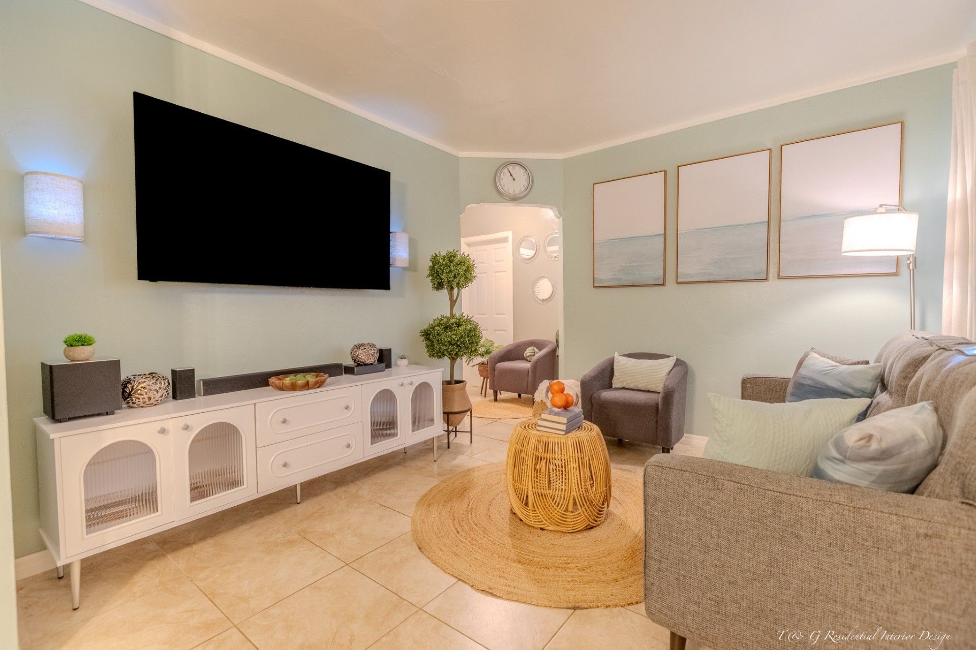 Living room with pale green walls, a mounted television, a white cabinet, two armchairs, and abstract art above the sofa.