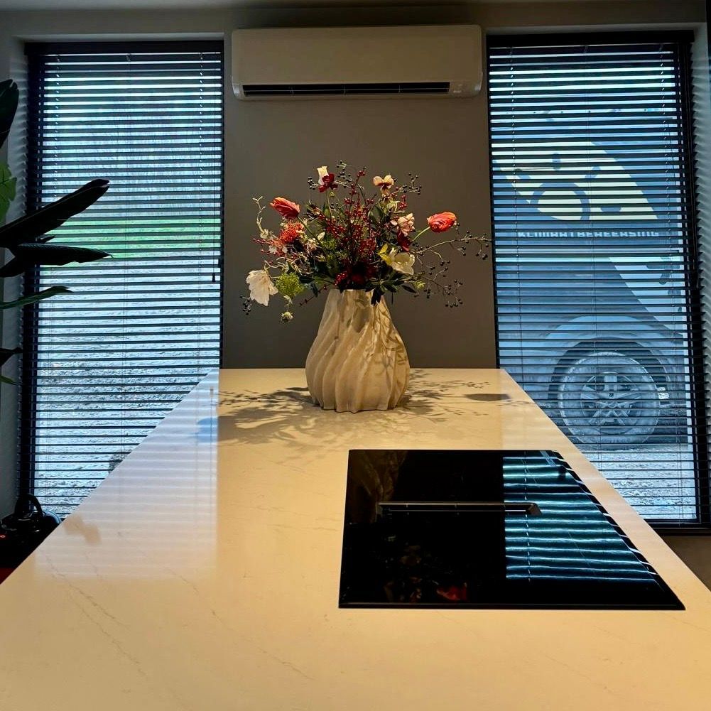 Wit keukeneiland met bloemen in een vaas, jaloezieën voor de ramen.
